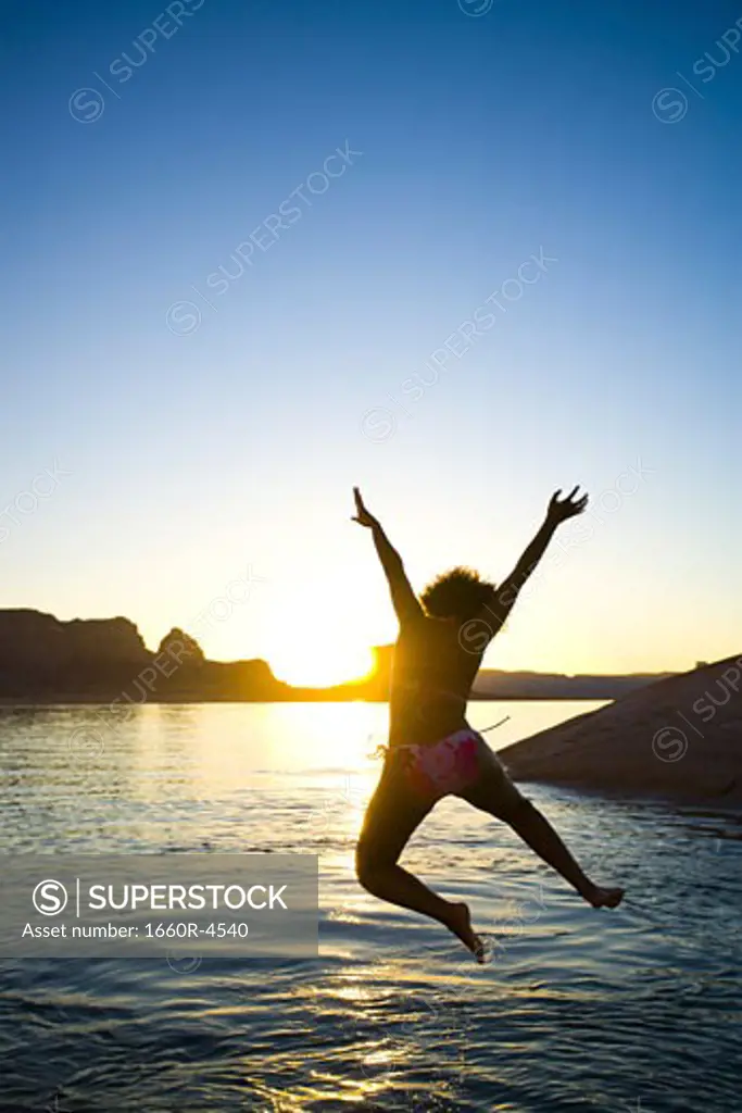 Rear view of a young woman jumping into a lake
