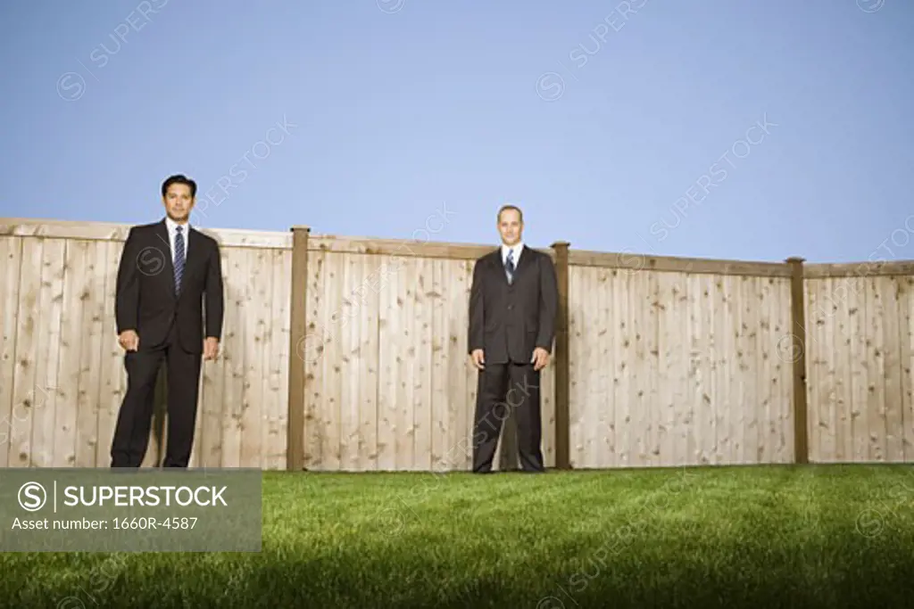 Low angle view of two businessmen standing in front of a fence