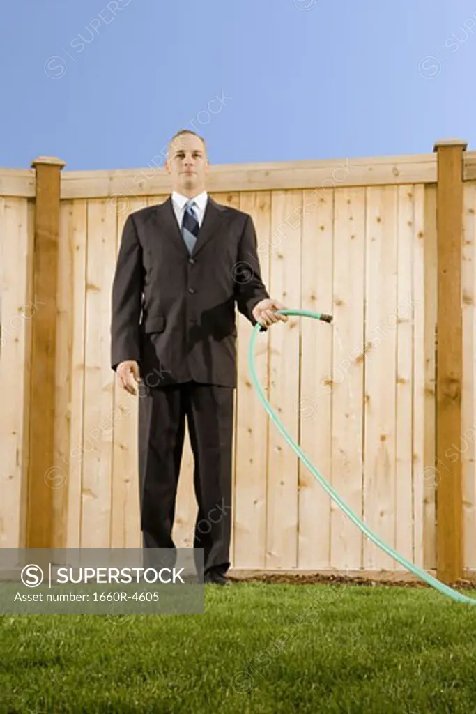 Low angle view of a businessman holding a hose standing in front of a wall