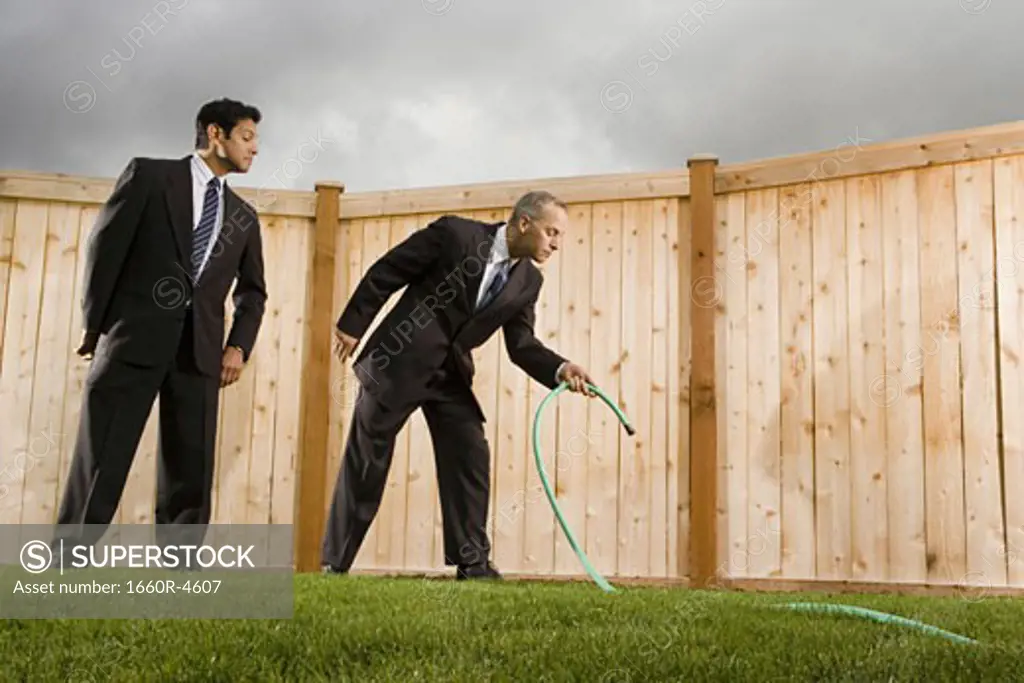 Low angle view of a businessman watering grass with another businessman looking at him