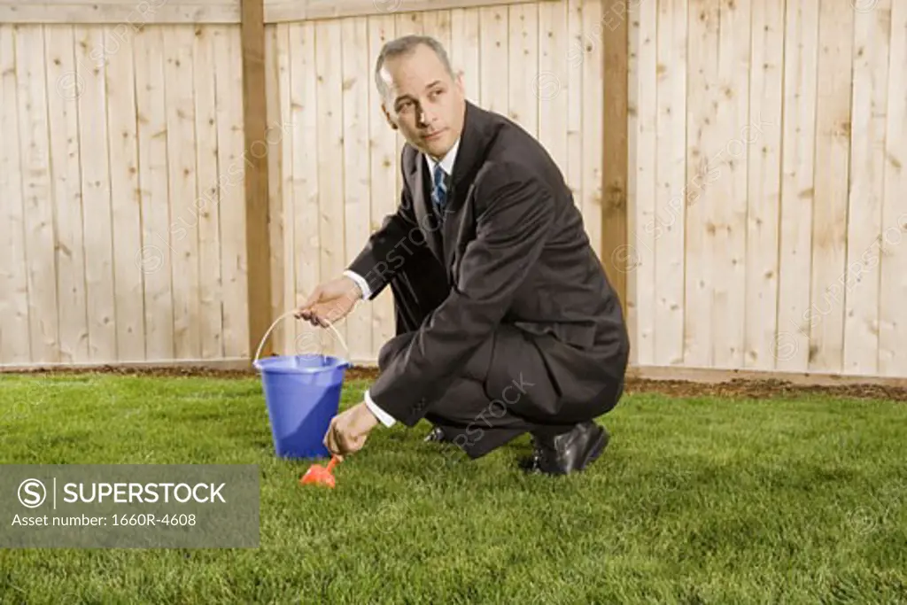 Profile of a businessman crouching on a lawn holding sand pail and shovel