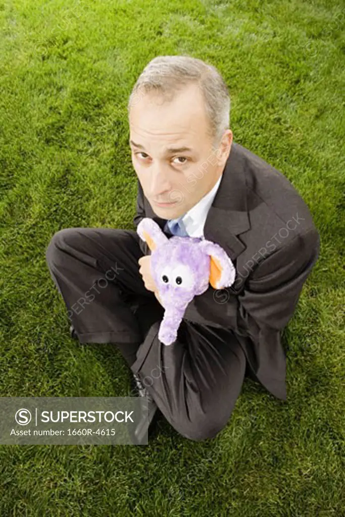 High angle view of a businessman with hugging a toy sitting on a lawn