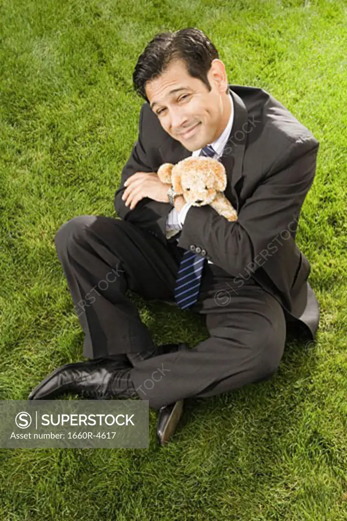 High angle view of a businessman with hugging a toy sitting on a grass