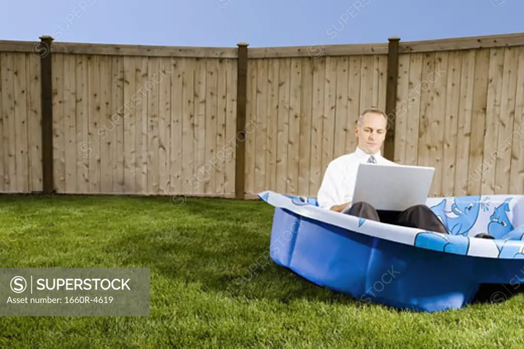 Mid adult man working on a laptop sitting in a wading pool