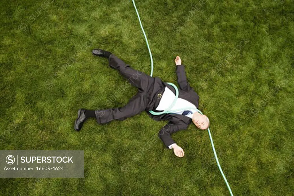 High angle view of a businessman with a hose lying down on a lawn