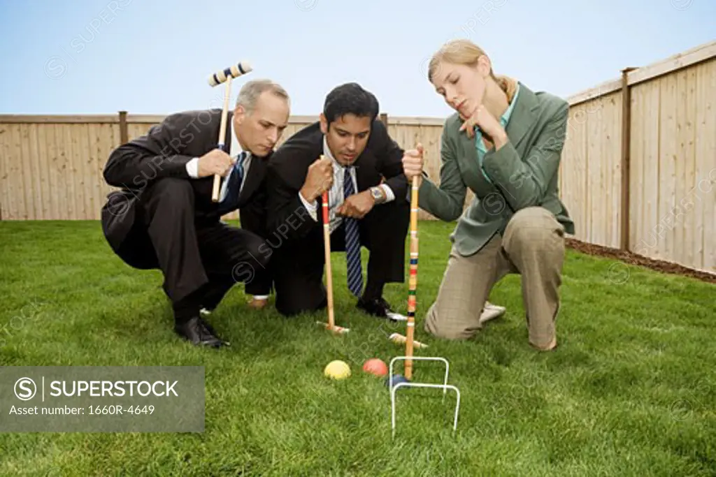 Two businessmen and a businesswoman playing croquet