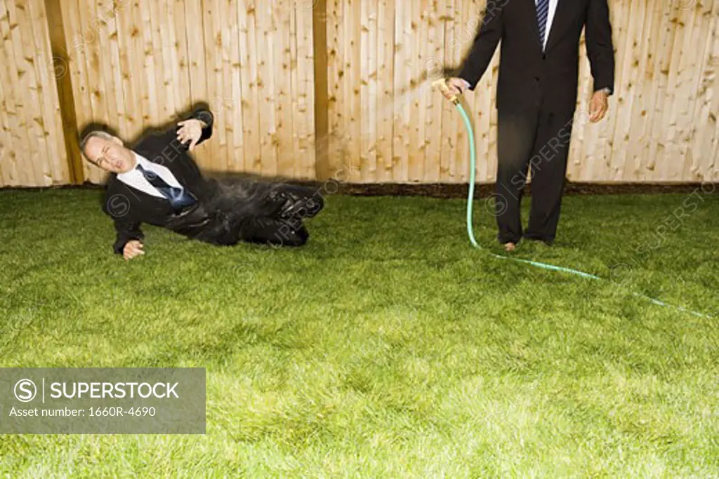 High angle view of a businessman sitting on a lawn getting hosed