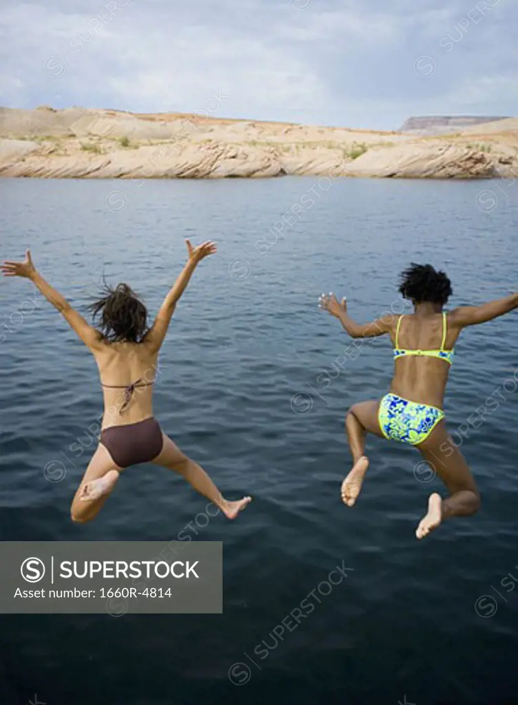 High angle view of two young women jumping into a lake