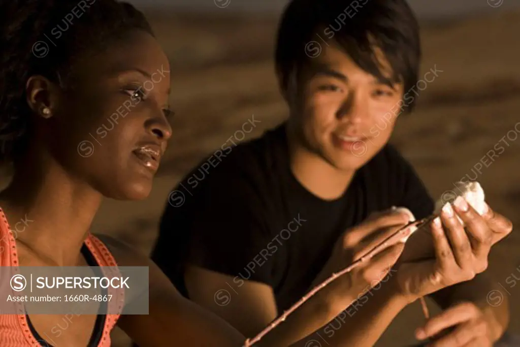 Close-up of a young woman putting marshmallows on a stick