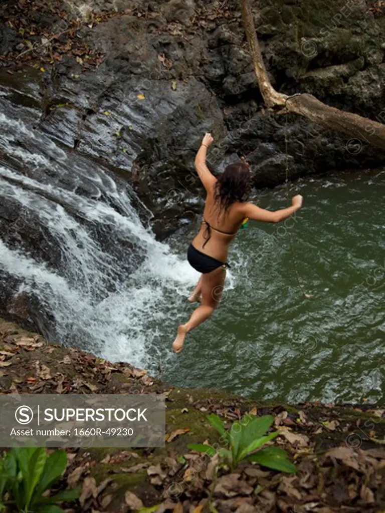 Costa Rica, Young woman jumping into pool by waterfall