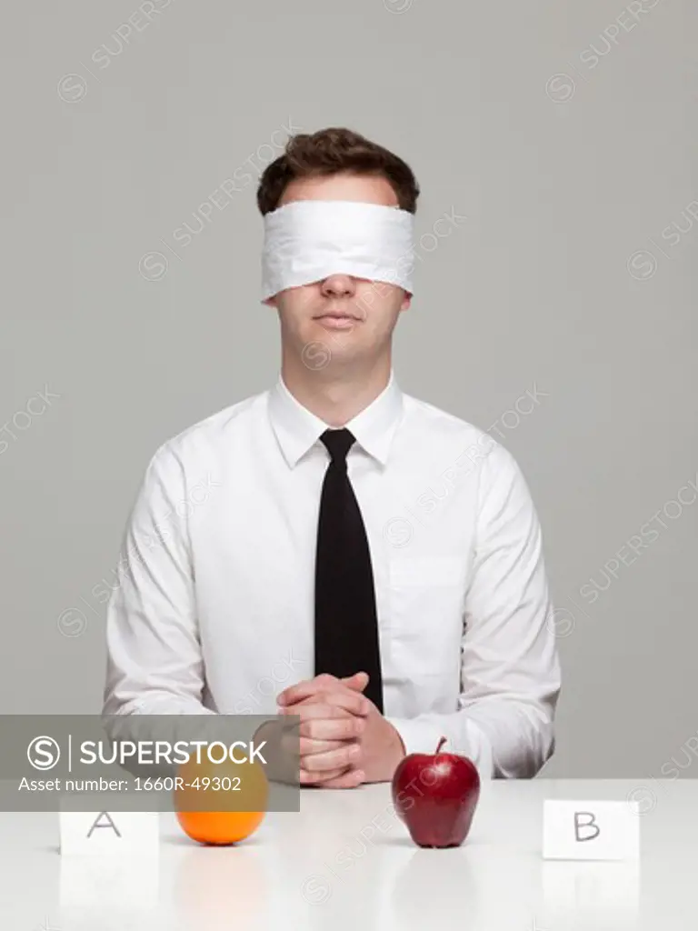 Studio portrait of young man with blindfold choosing between orange and apple