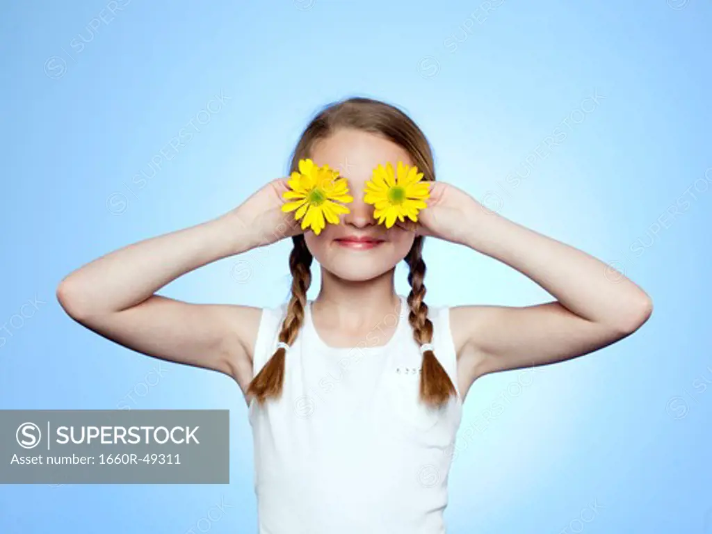Studio portrait of girl (10-11) shielding eyes by two yellow flowers