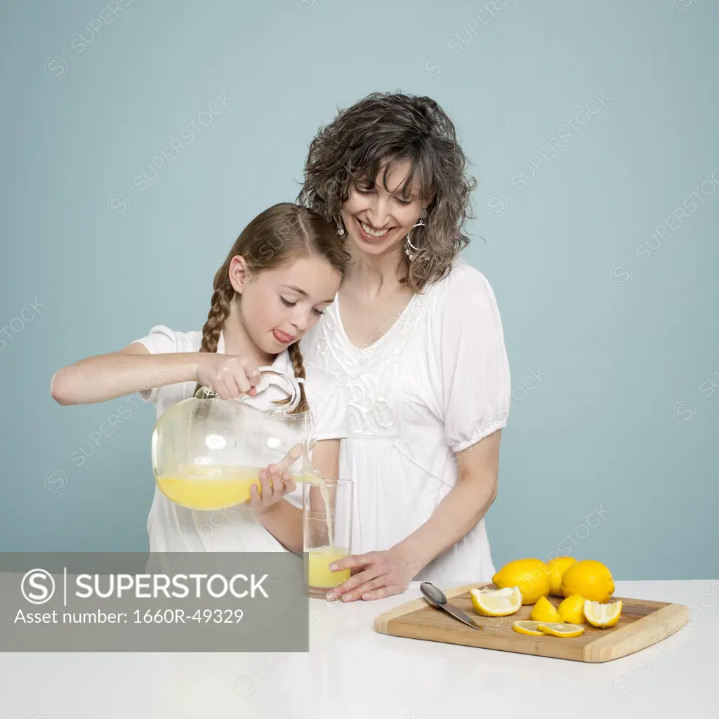 Studio shot of mother assisting daughter (10-11) pouring lemonade