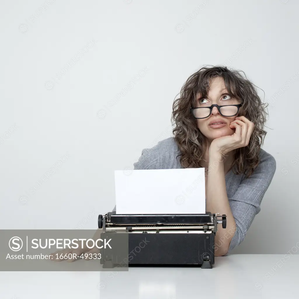 Studio shot of bored woman sitting at table with typewriter