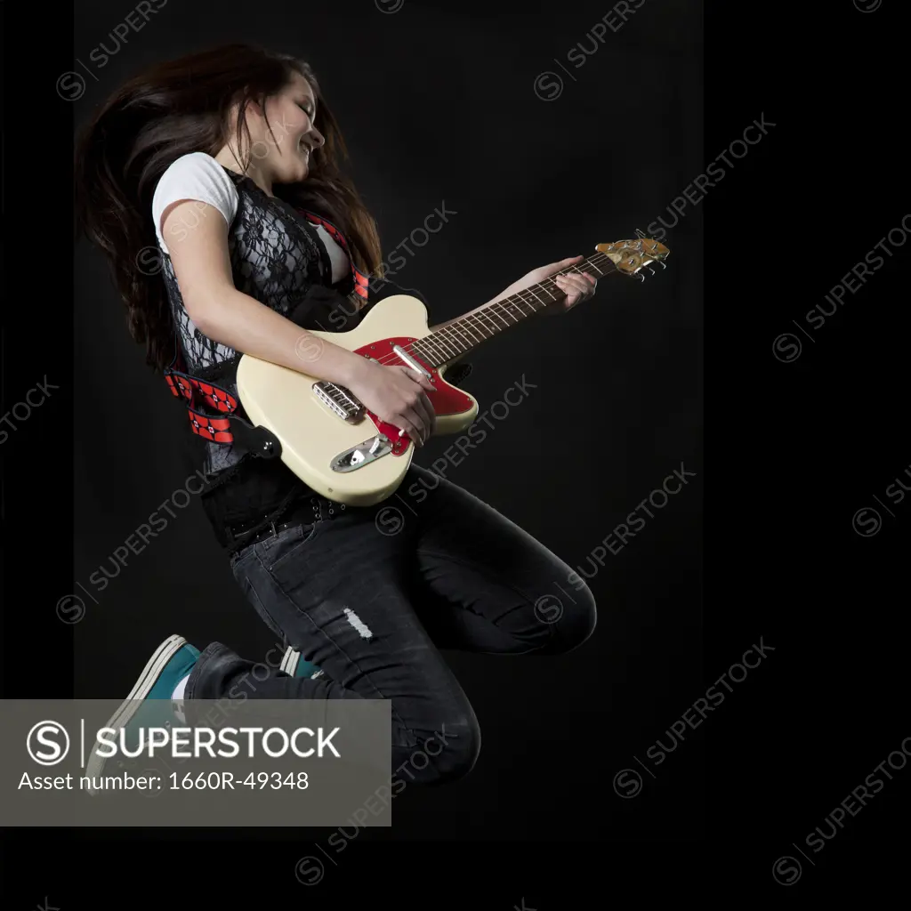 Studio shot of teenage girl (14-15) playing electric guitar and jumping