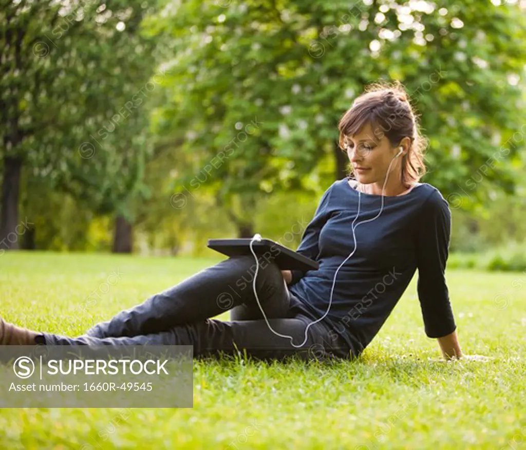 UK, London, Young woman sitting in park and using digital tablet