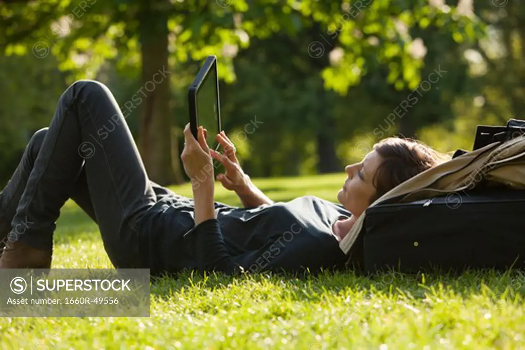 UK, London, Woman lying on grass using tablet