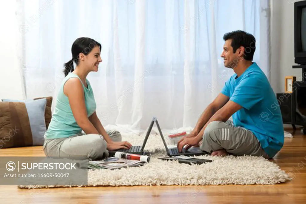 Man and woman lying on carpet with laptops