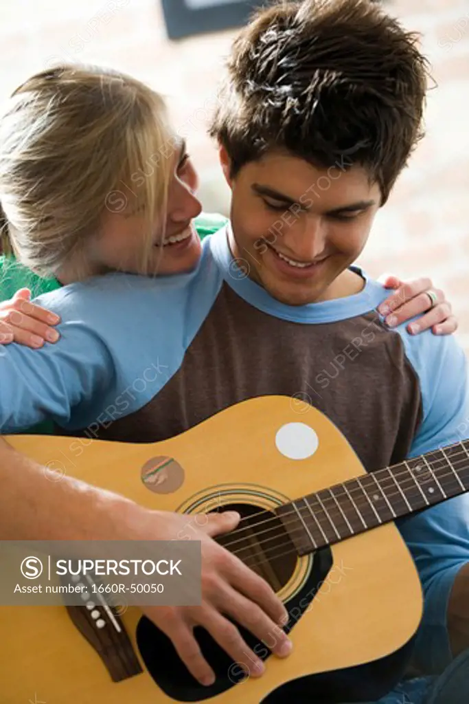Man playing guitar and singing for woman on sofa