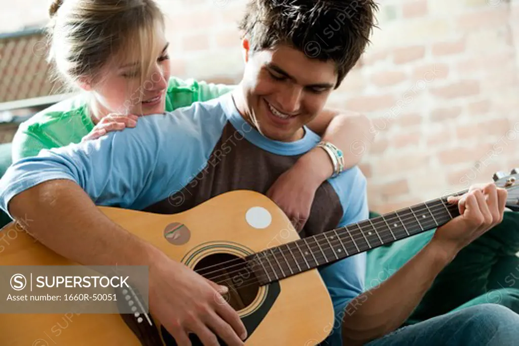 Man playing guitar and singing for woman on sofa