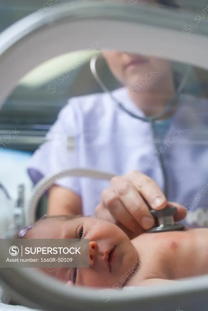Nurse examining newborn in incubator