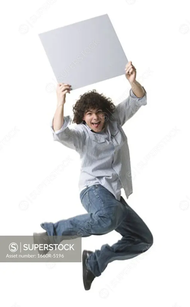 Portrait of a teenage boy holding a blank sign and jumping in mid-air