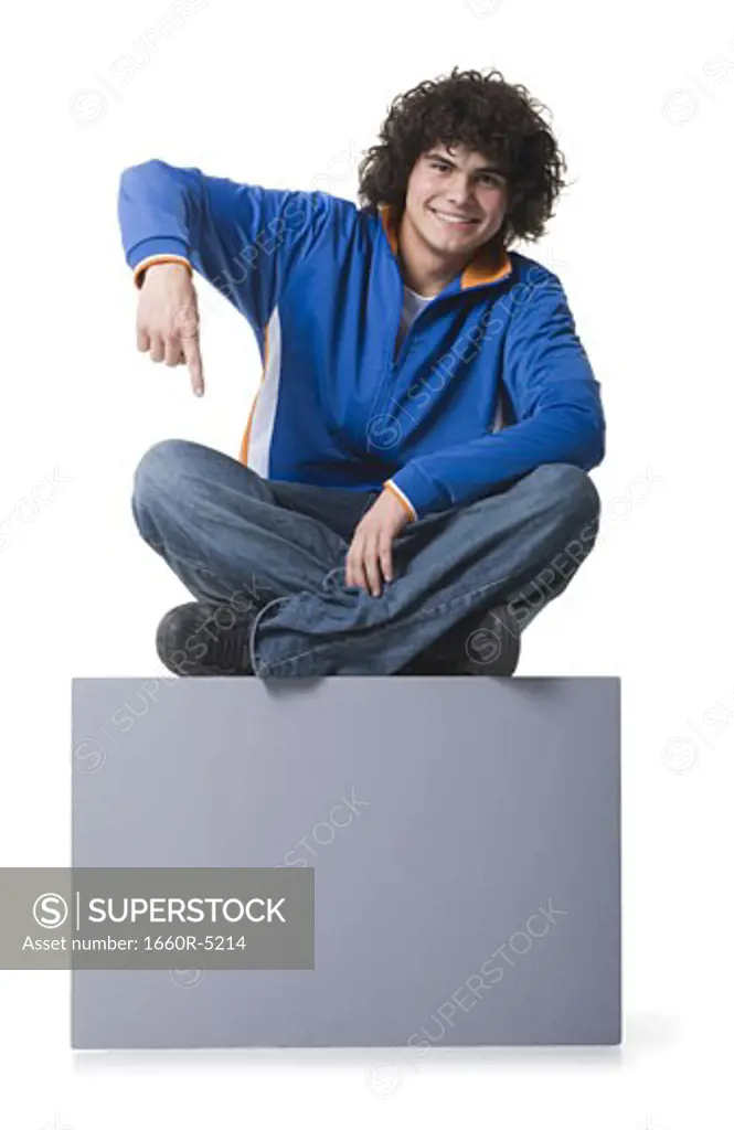 Portrait of a teenage boy sitting on a blank sign and pointing