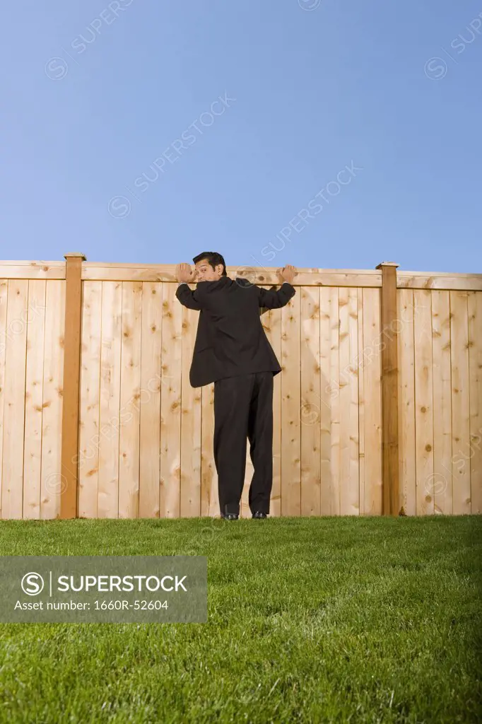 Businessman looking over a wooden fence