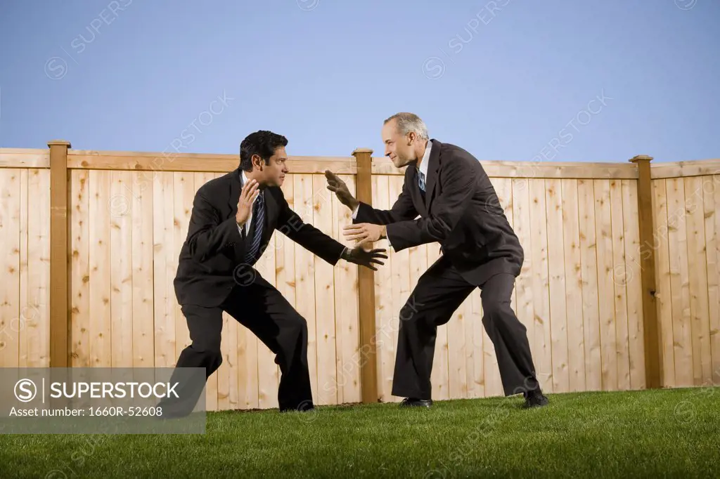 Businessmen in front of a fence playfighting