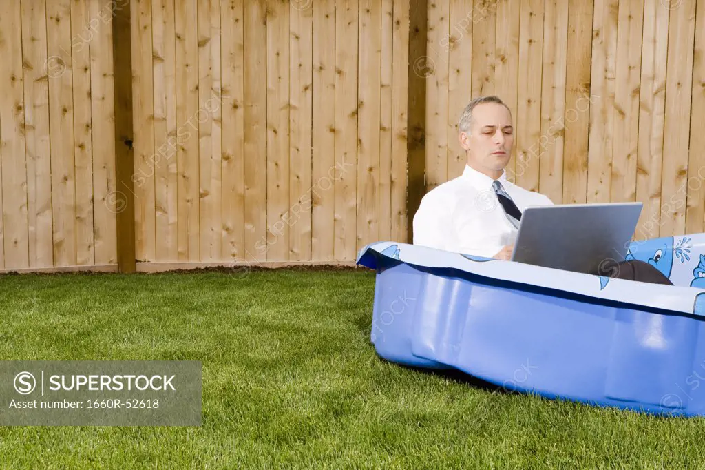 Businessman in a backyard pool on a laptop
