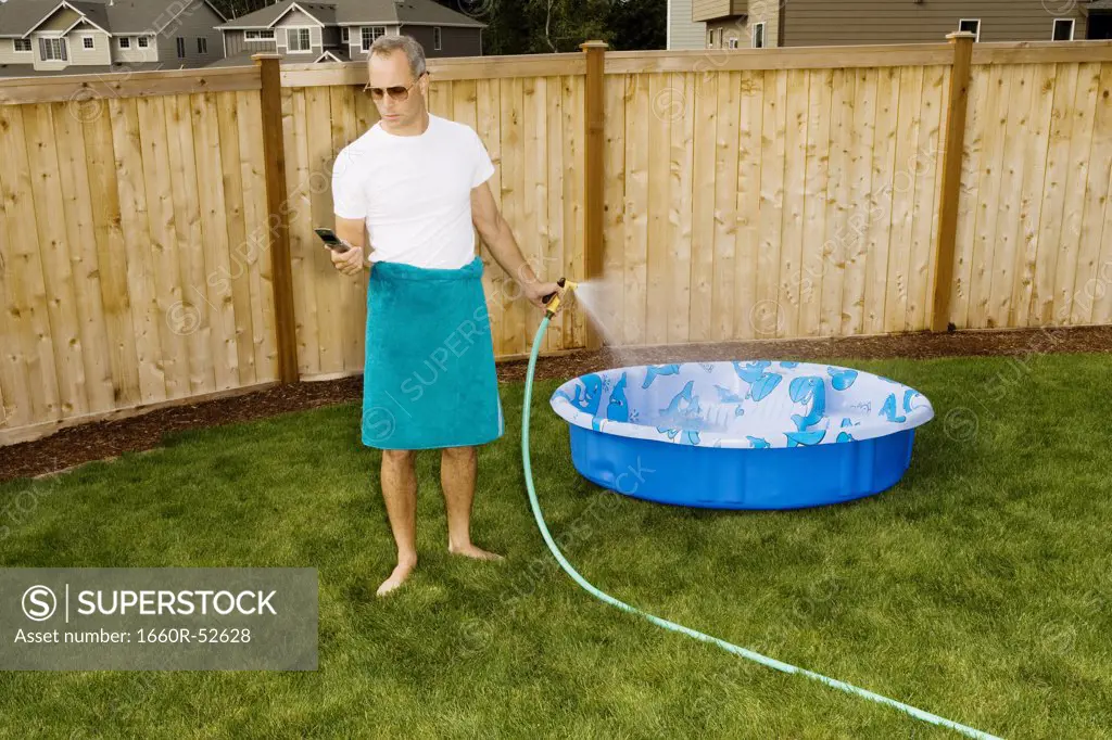 Man in yard with cell phone and hose
