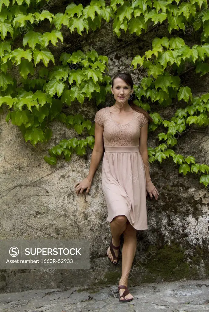 Italy, Ravello, Portrait of woman in dress leaning overgrown wall