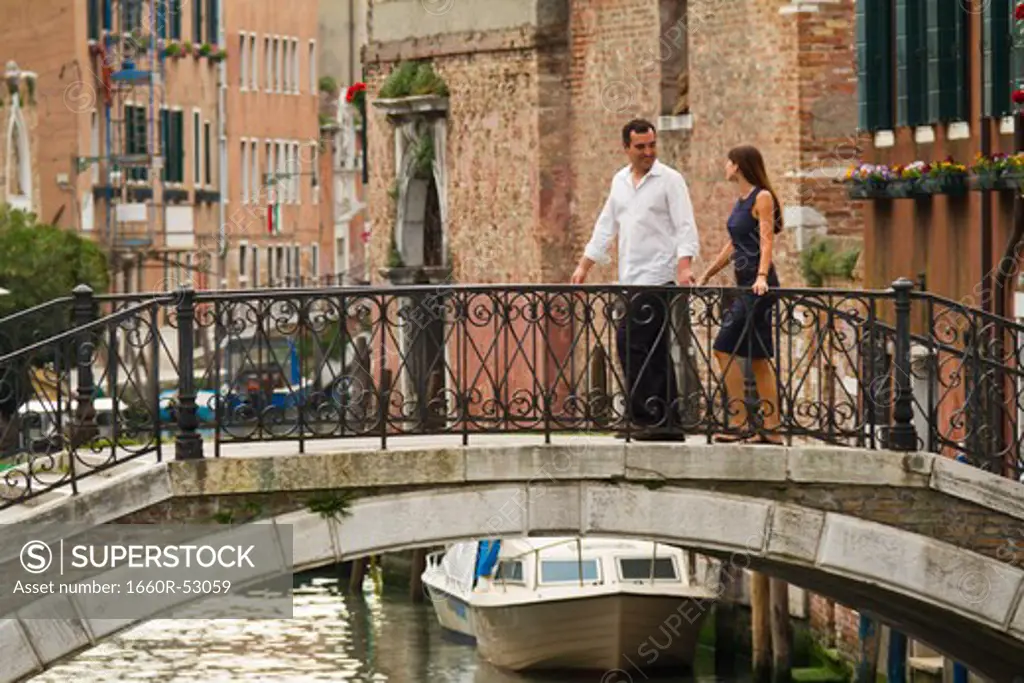 Italy, Venice, Mature couple holding hands and walking through bridge