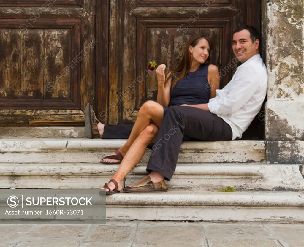 Italy, Venice, Mature couple sitting together at steps, woman holding red rose