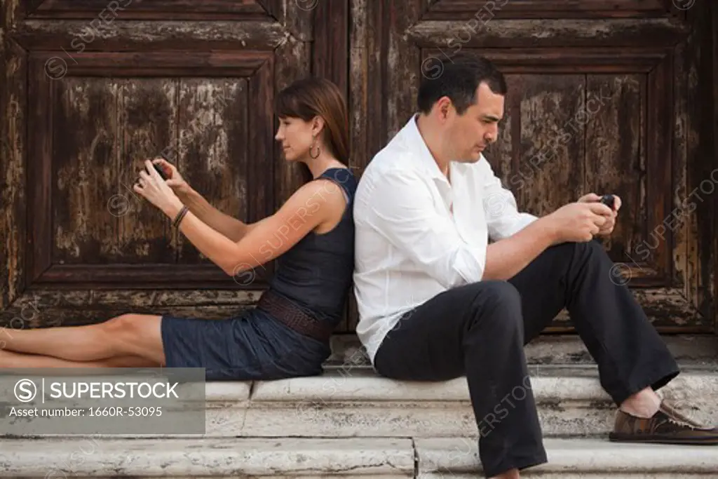 Italy, Venice, Couple sitting on steps, using smart phones