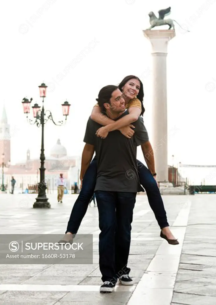 Italy, Venice, Young man giving piggyback ride to woman on St. Mark's Square