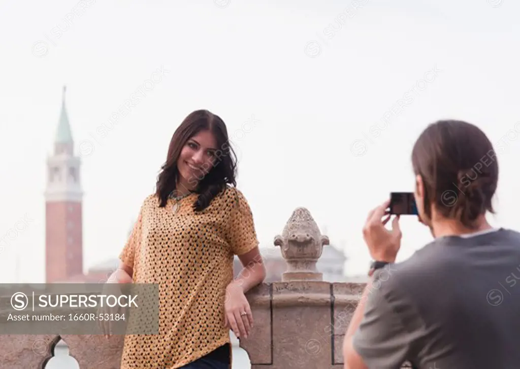 Italy, Venice, Young man photographing woman on bridge San Giorgio Maggiore church in background