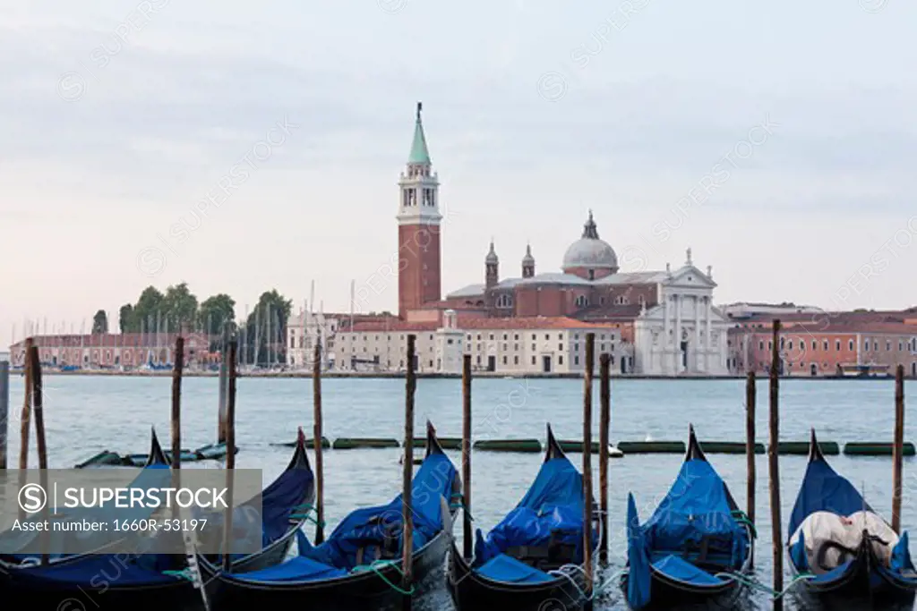 Italy, Venice, Young couple embracing by lagoon, gondolas and San Giorgio Maggiore church in background