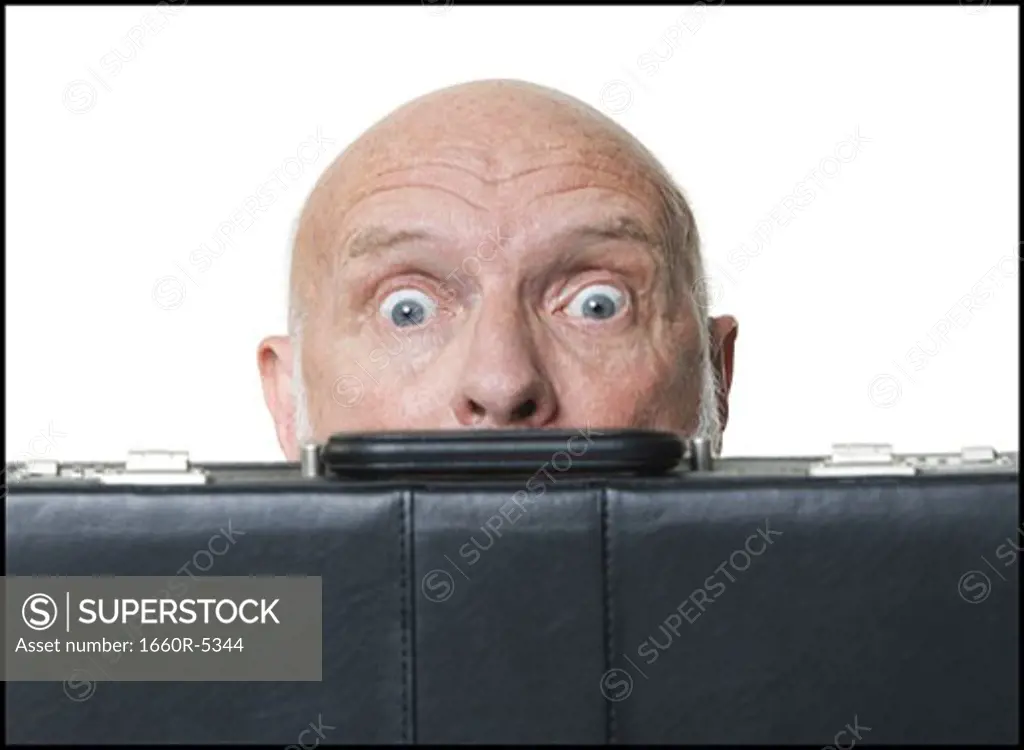 Portrait of a businessman hiding himself behind a briefcase
