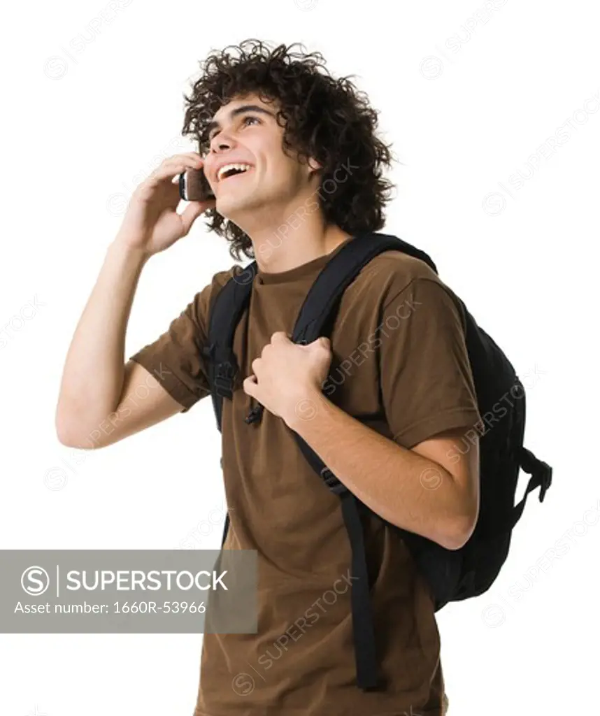 Teenage boy talking on cell phone holding backpack