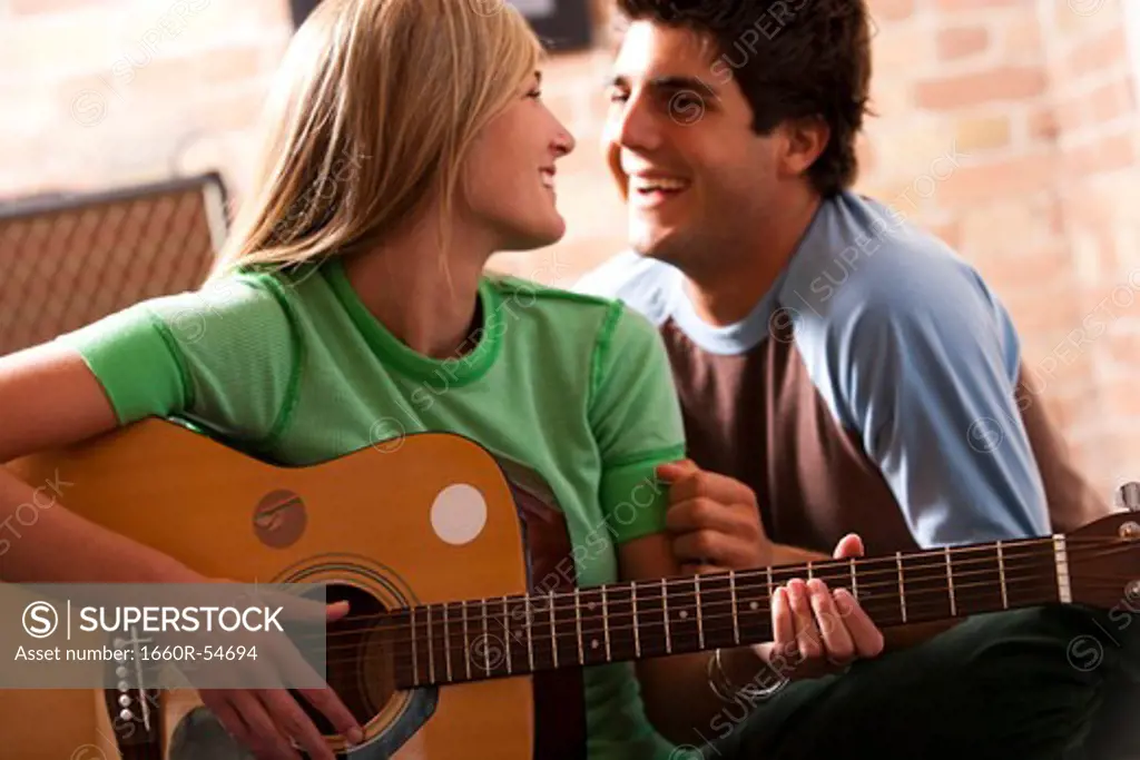 Woman playing guitar with man watching