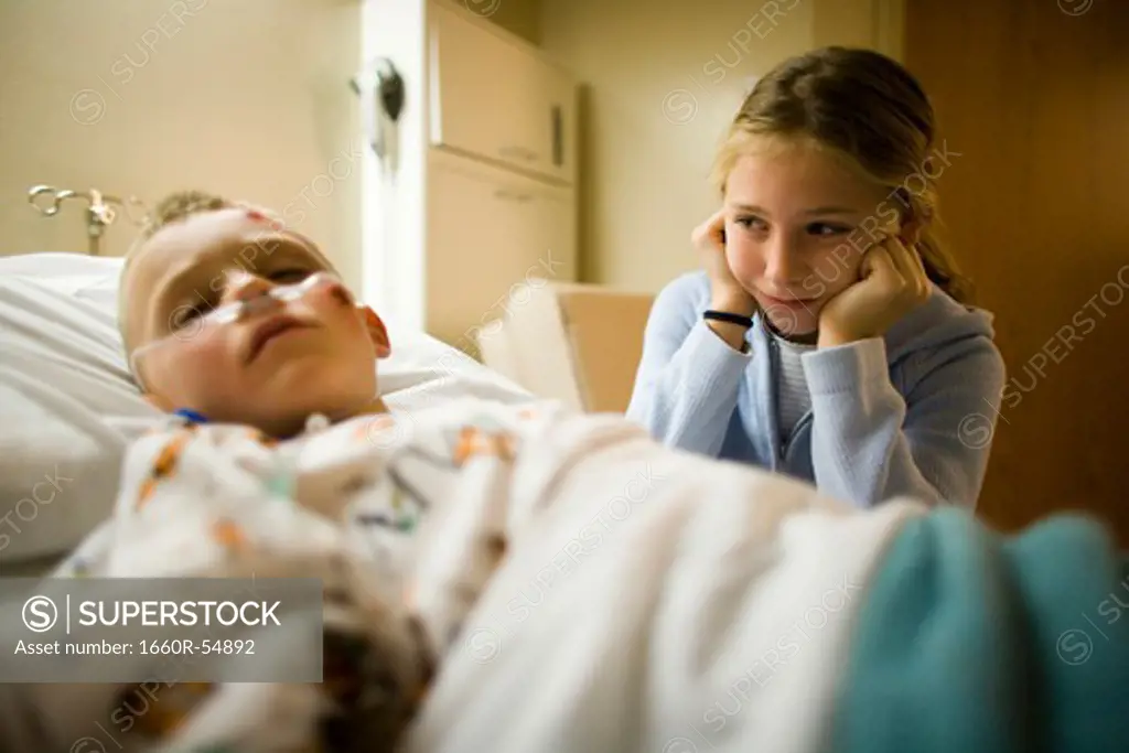 Young girl sitting by brother in hospital bed