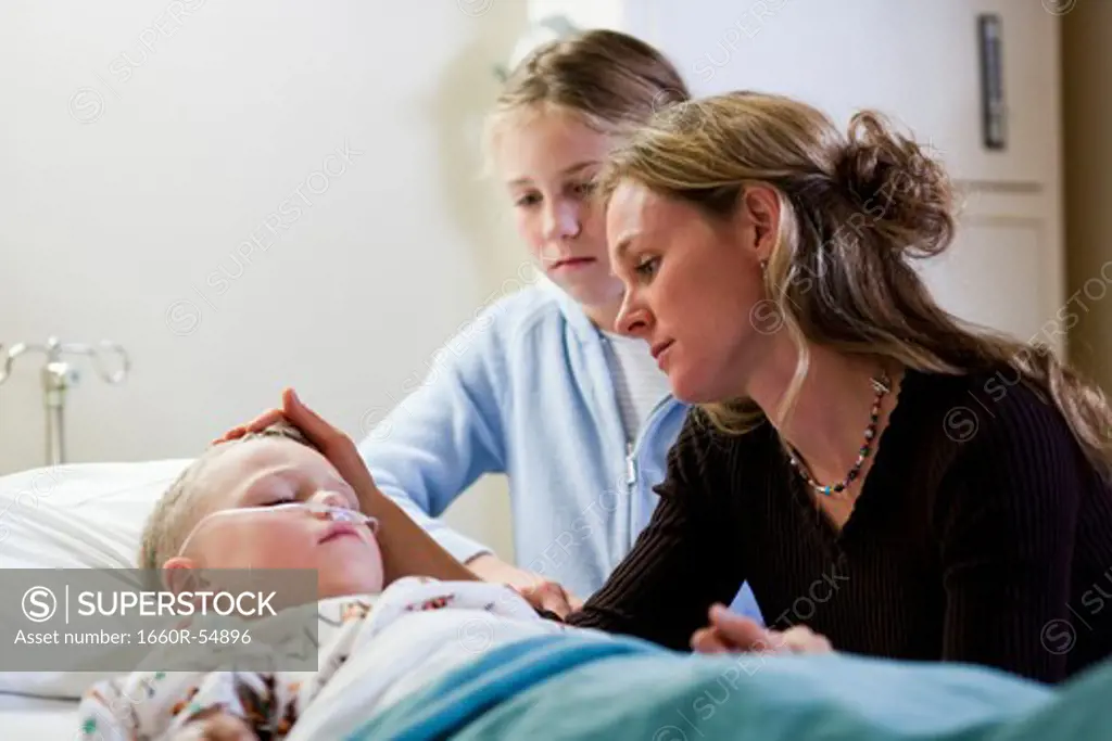 Mother and daughter sitting by young boy's hospital bed