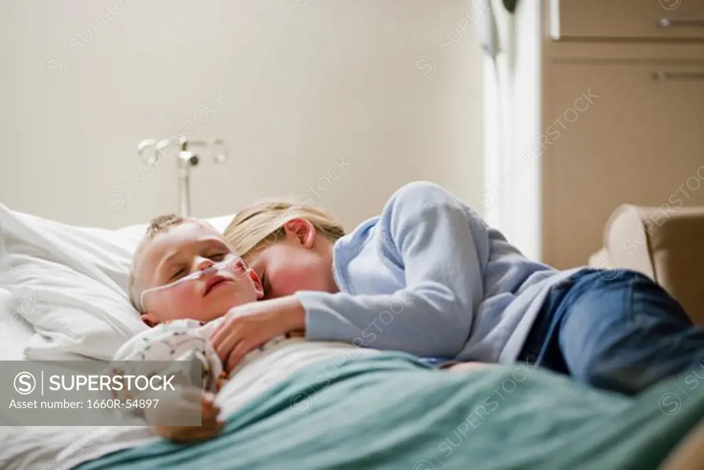Girl laying with brother on hospital bed