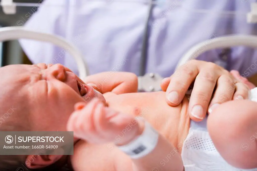 Nurse examining crying newborn in incubator