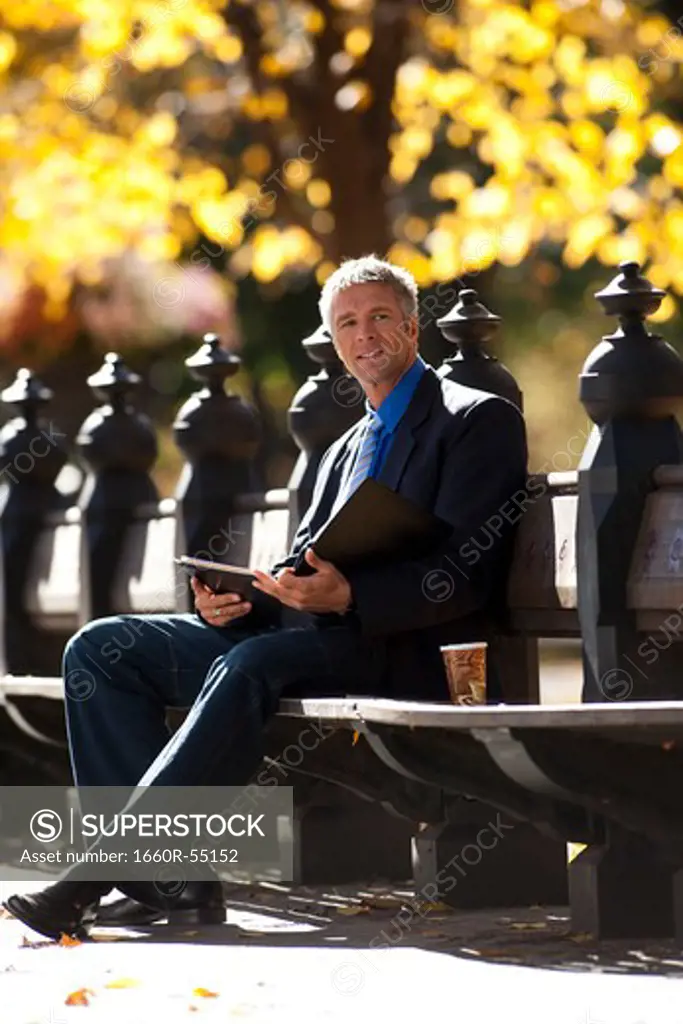 Businessman on wooden bench outdoors with newspaper
