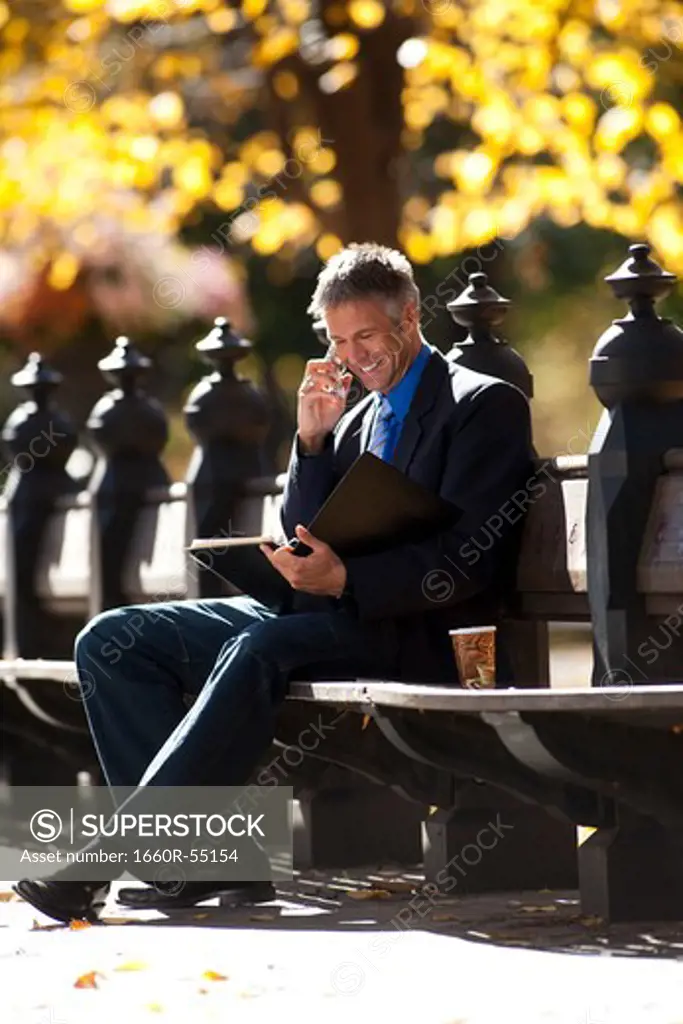 Businessman on wooden bench outdoors with newspaper