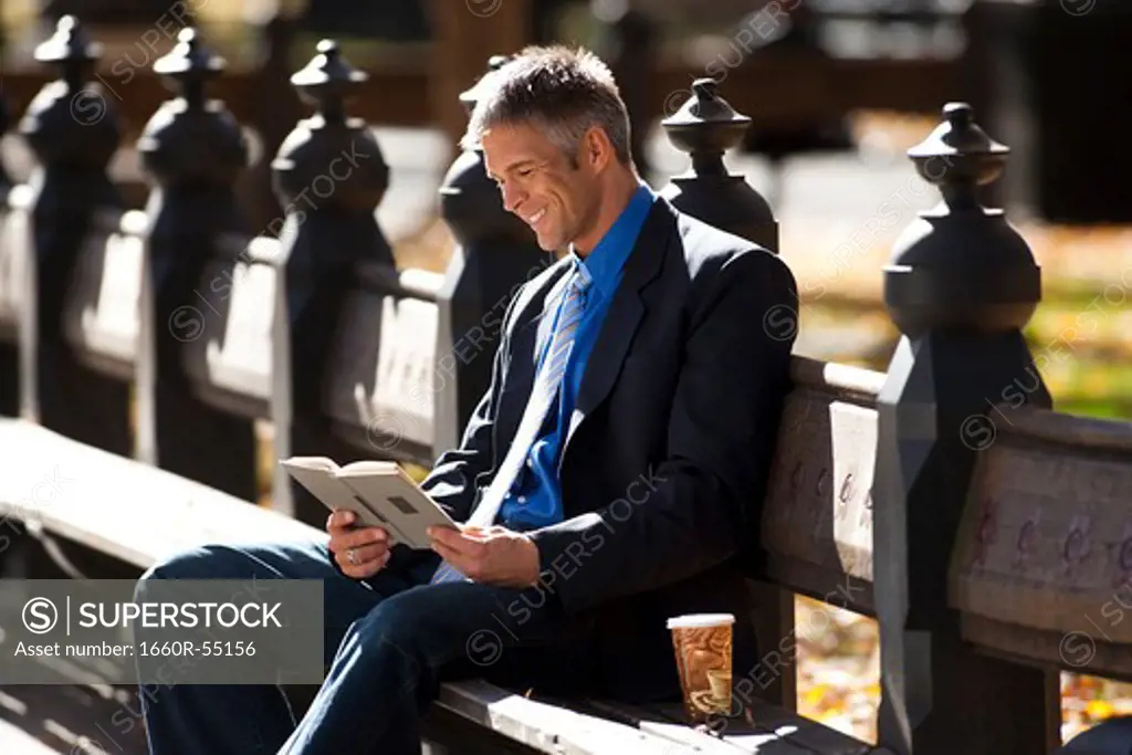 Businessman on wooden bench outdoors with book