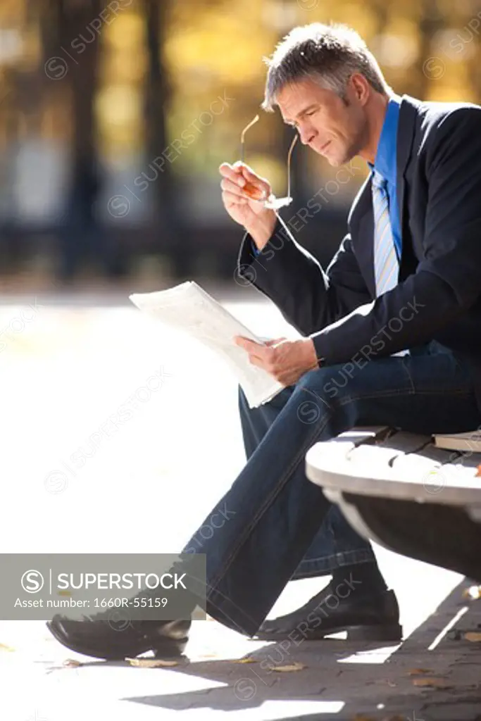 Businessman on wooden bench outdoors with book