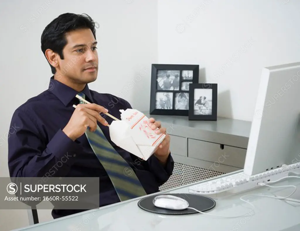 Male sitting at desk with computer and Chinese take out
